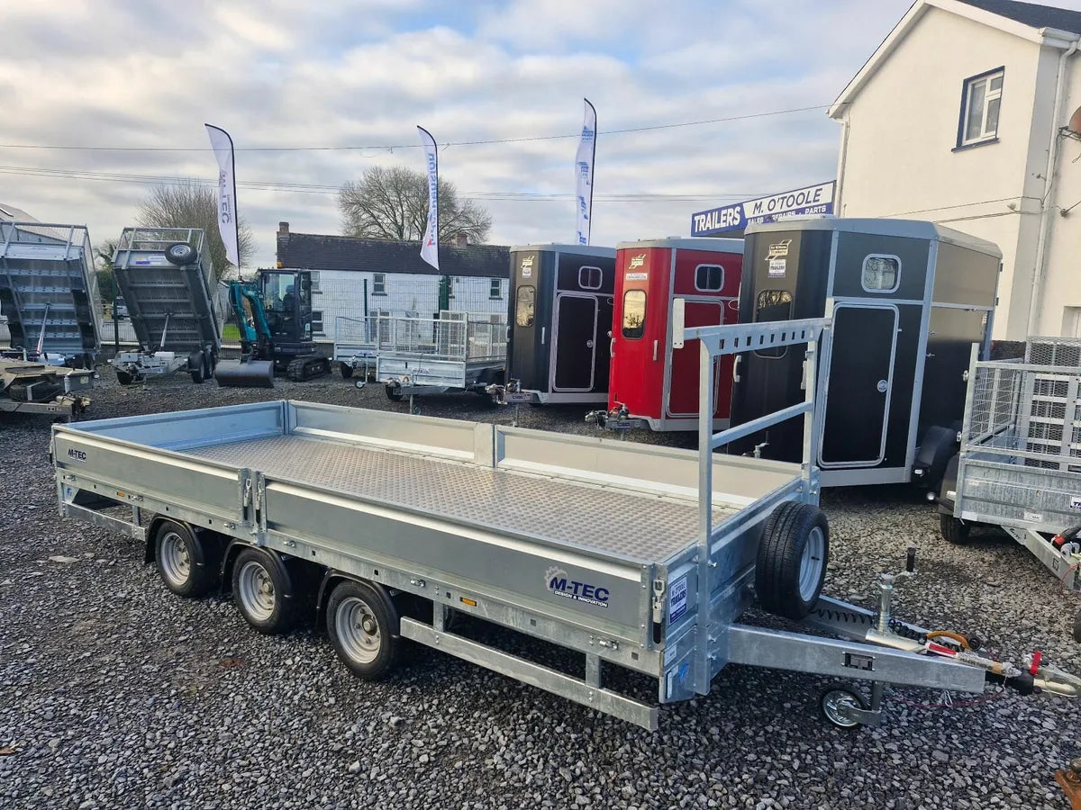 Metal trailer with 'M-Tec' branding on a gravel surface with other trailers in the background.